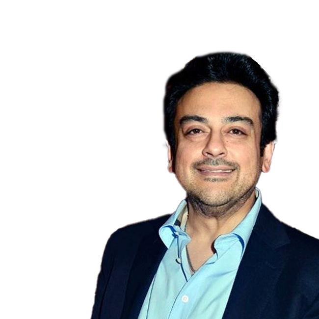 Adnan Sami smiling, wearing a blue shirt and dark blazer against a dark background