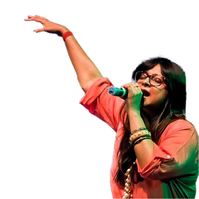 Dominique Cerejo, in an orange outfit and glasses, performing on stage with a raised arm