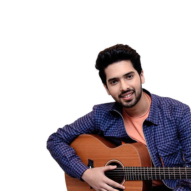 Armaan Malik holding a guitar and smiling, wearing a blue checkered shirt and orange t-shirt.