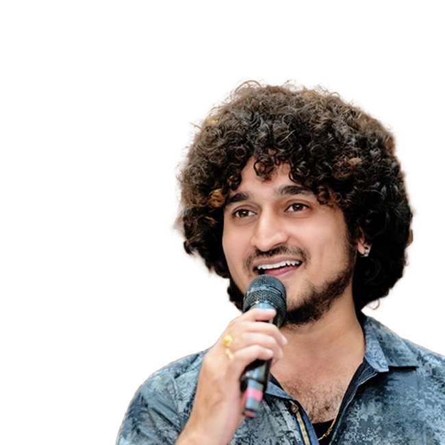 Arun holding a microphone and smiling, wearing a patterned dark blue shirt.